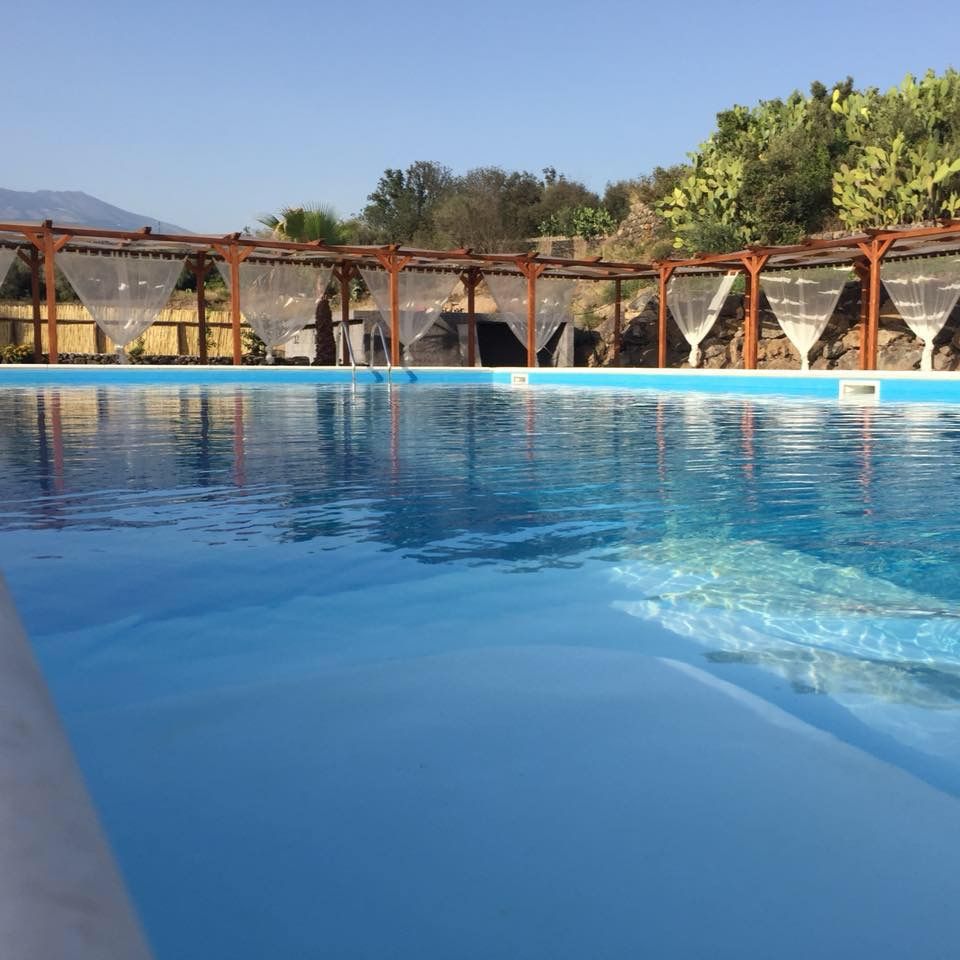 L'acqua turchese della piscina davanti al muretto in pietra lavica con i fichi d'India