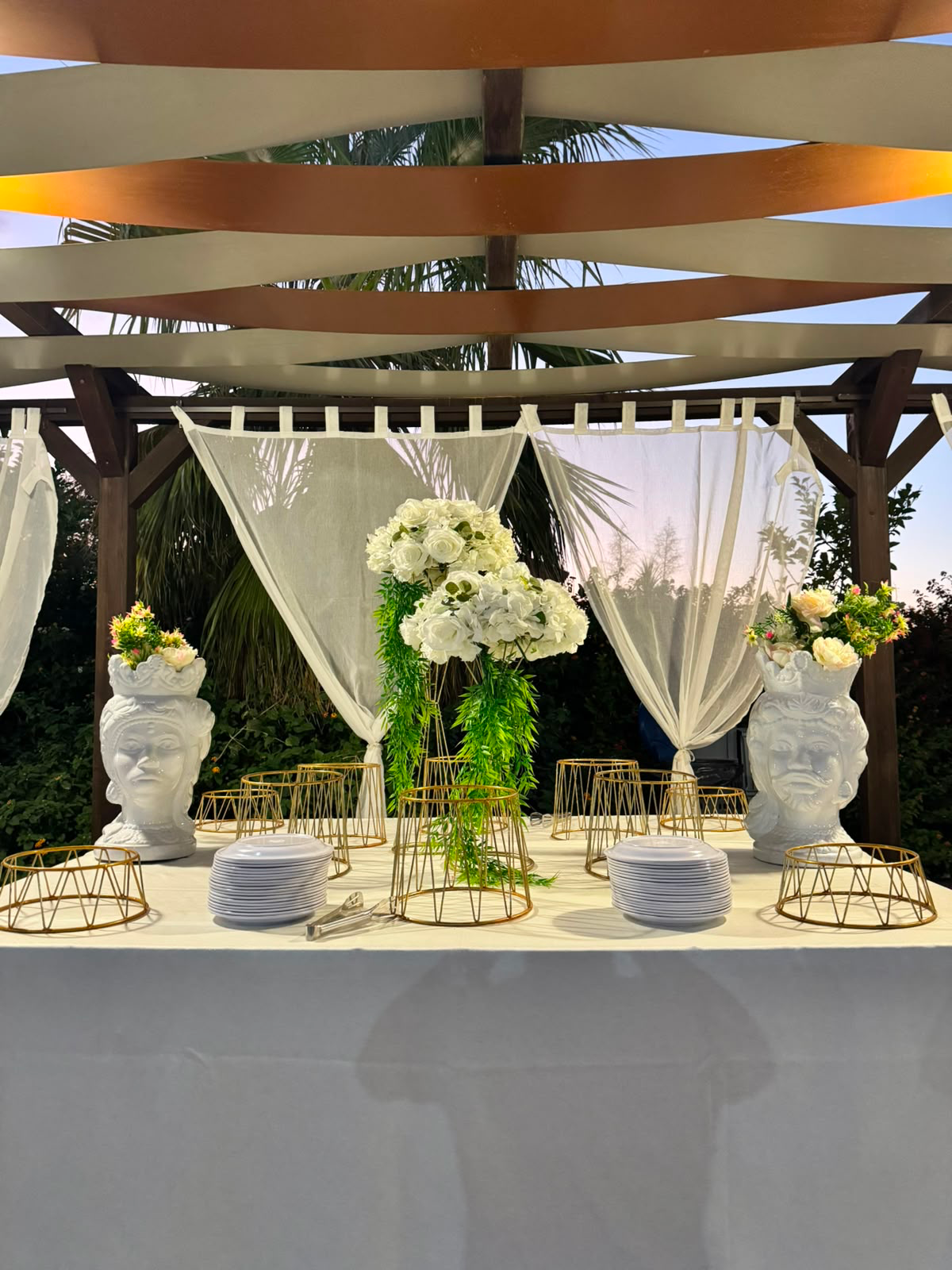 Il buffet di un evento con le teste di moro siciliane e i fiori bianchi, sotto il pergolato
