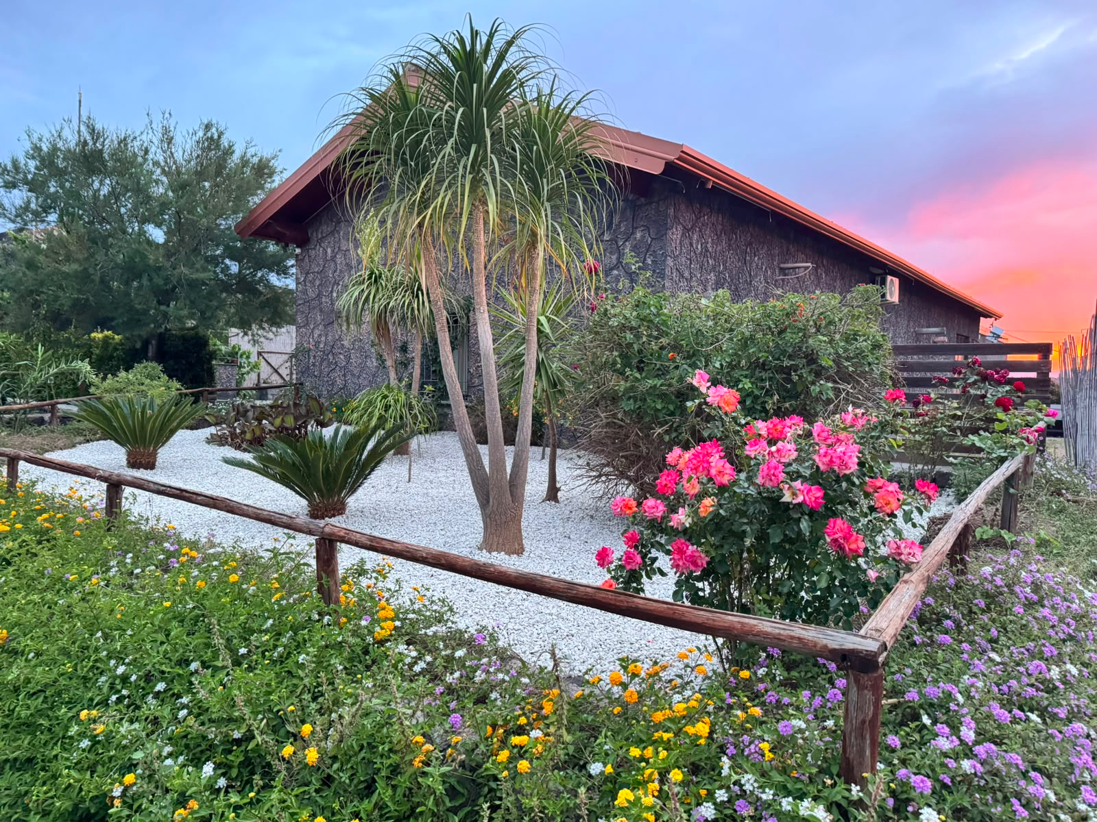 Il casale in legno tra i fiori del giardino, con il cielo rosa del tramonto