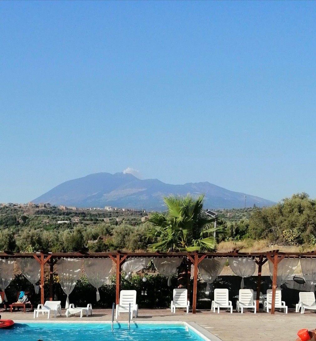 La piscina all'aperto de Il Sole dell'Etna con i lettini bianchi e, sullo sfondo, l'Etna che fuma