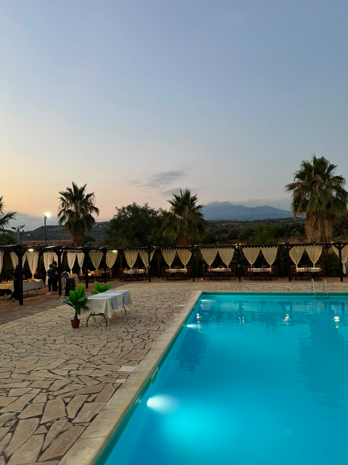 La piscina illuminata al tramonto, con le palme e i gazebo intorno